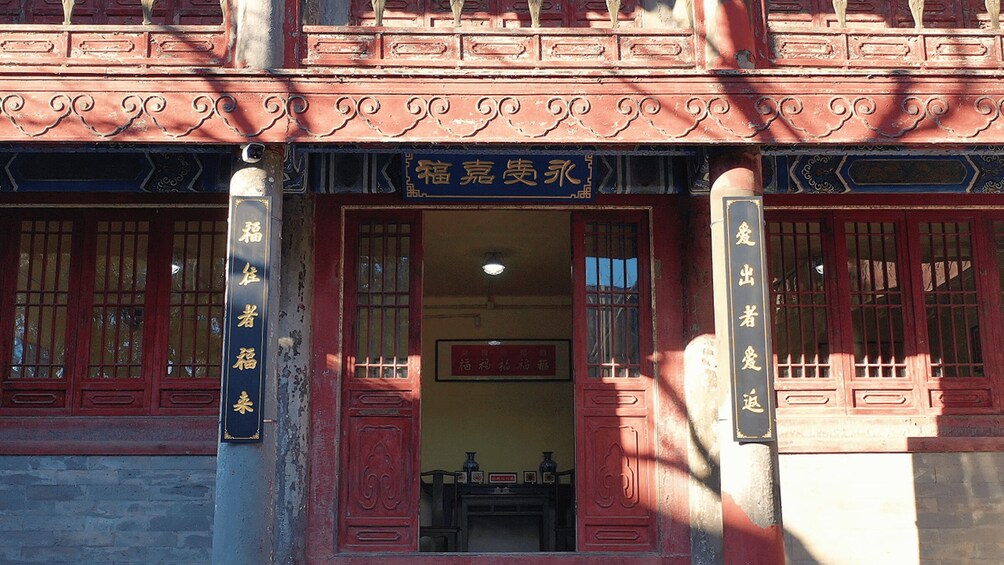 A traditional building with ornate red doors and windows, featuring Chinese characters and a signboard. 2