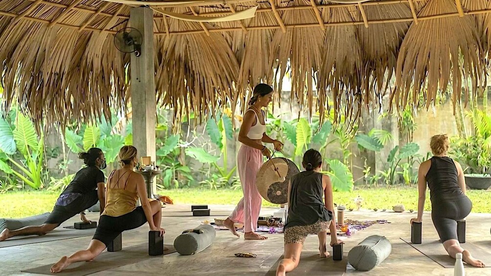 A group of people practicing yoga outdoors under a thatched roof. 1