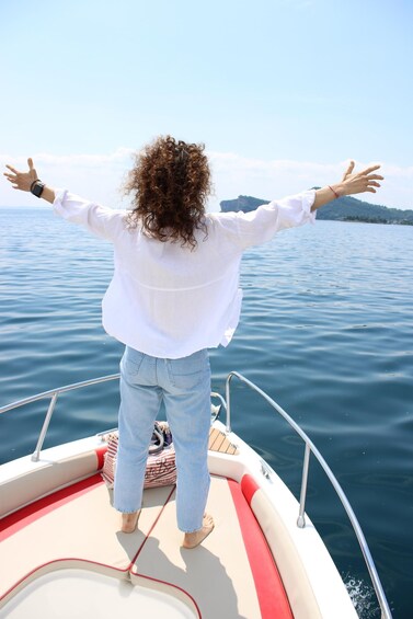 A person standing on a boat with arms outstretched, facing a calm body of water. 1