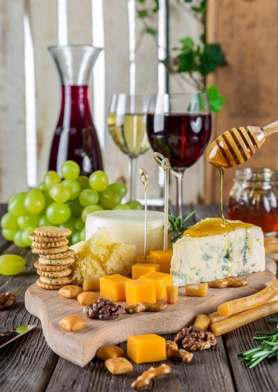 A variety of cheeses, crackers, grapes, and nuts on a wooden board with glasses of wine in the background. 1