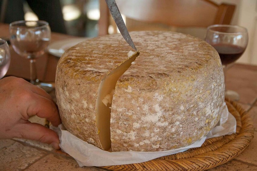 A round cheese with a knife inserted into it, placed on a woven basket. 4