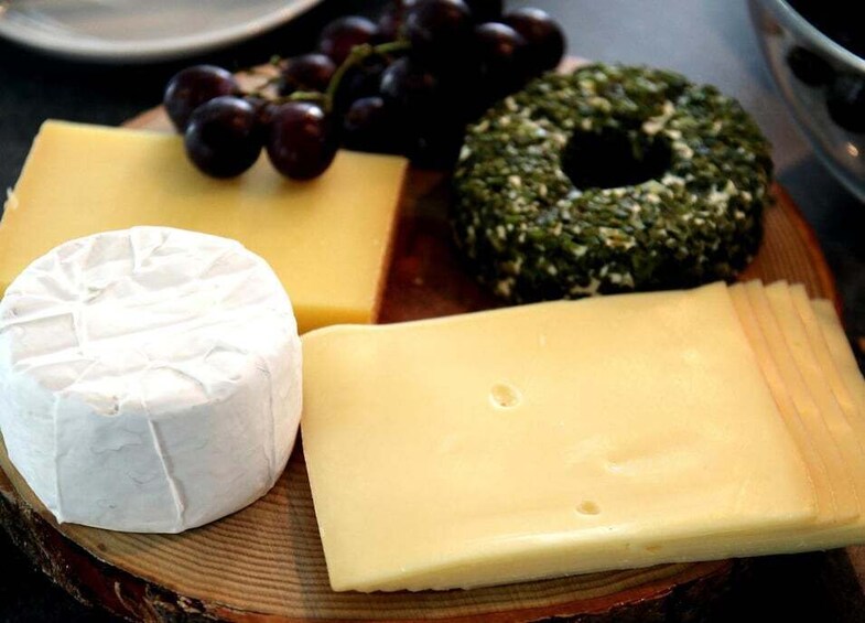 A wooden board with three types of cheese, a round cheese, a wedge of cheese, and a leafy cheese. 5