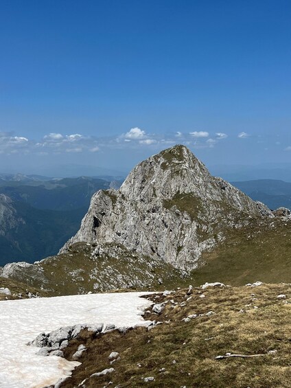 A rugged mountain peak with a snow patch in the foreground and a clear blue sky. 2