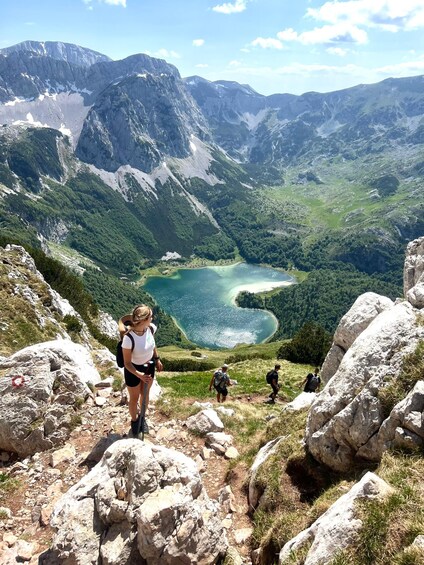 Hikers on a mountain trail with a lake and forested valley in the background. 4