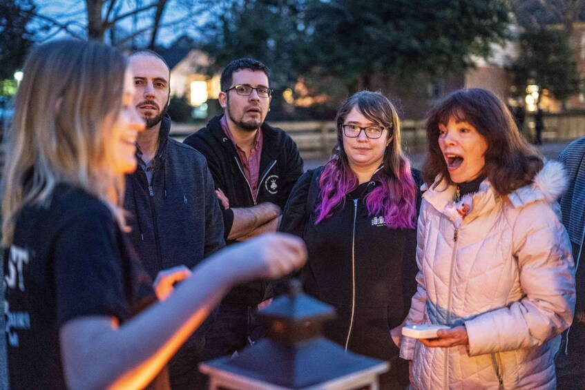 A group of people outdoors at dusk, some holding objects, with trees and a building in the background. 5
