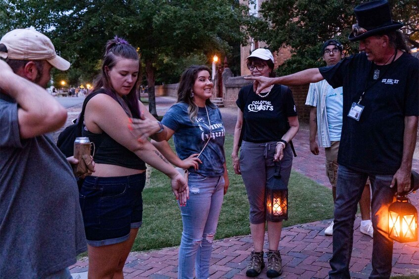 A group of people outdoors at dusk, some holding drinks and lanterns, with trees and a brick pathway in the background. 4