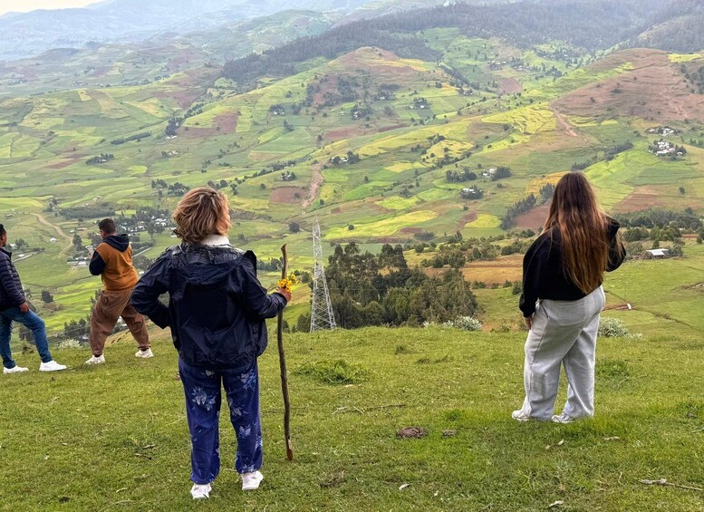 A group of people standing on a grassy hill overlooking a valley with fields and a power line tower. 2