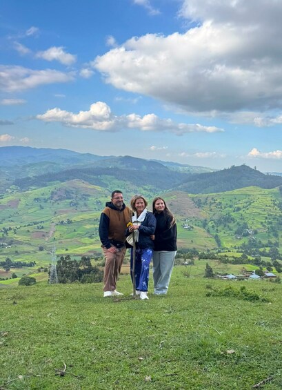 Three people standing on a grassy hill with a mountainous landscape in the background. 3