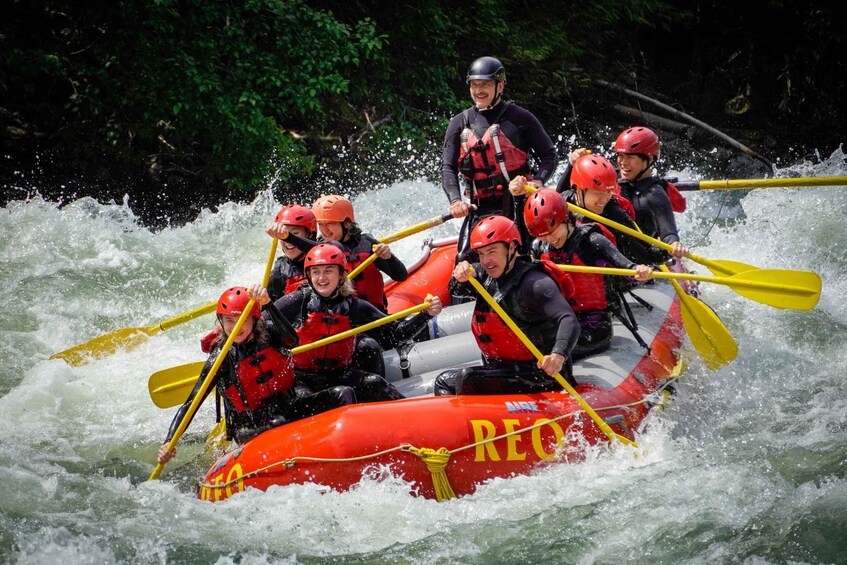 A group of people in a red inflatable raft with yellow paddles, navigating through white water rapids. 4
