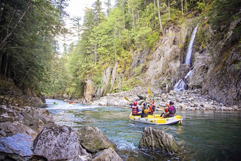 A group rafting down a river surrounded by forested cliffs and a waterfall. 3
