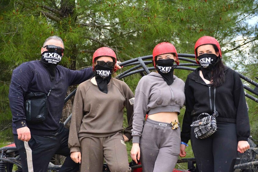 Four people wearing helmets and protective gear, standing near a tree with a metal structure behind them. 3