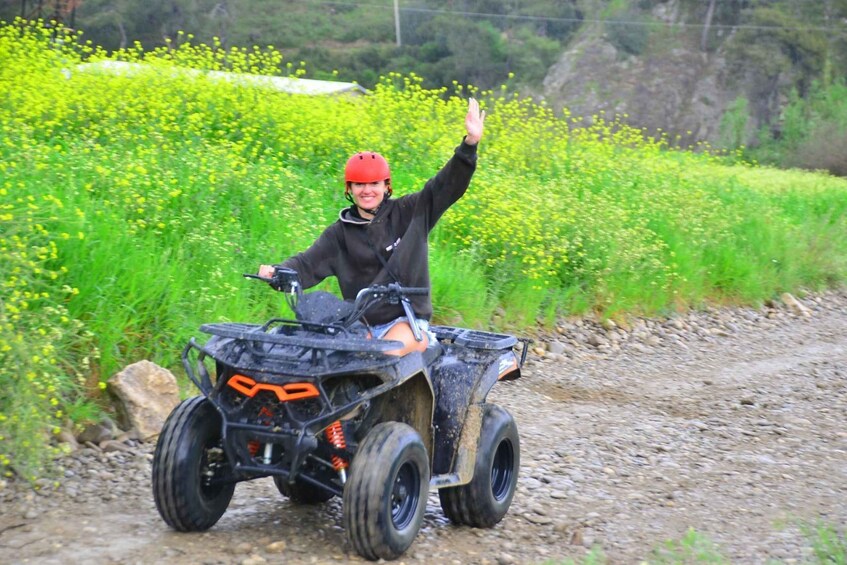 A person riding an ATV on a dirt path with yellow flowers and green vegetation in the background. 4
