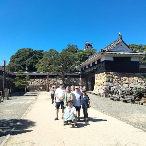 A group of people standing in front of a traditional Japanese building with a stone wall and a tiled roof. 5