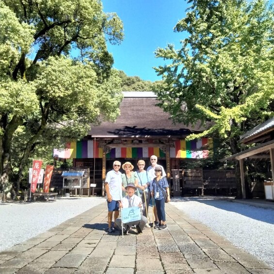 A group of people posing in front of a traditional Japanese building with a tiled roof and colorful flags. 4