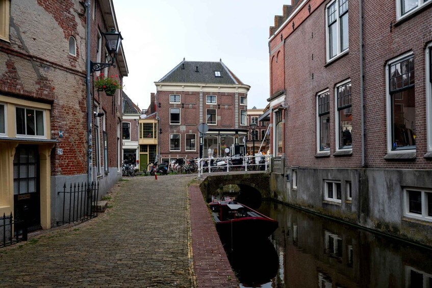 A narrow canal with a red boat docked on the right, flanked by historic brick buildings with a bridge in the background. 3