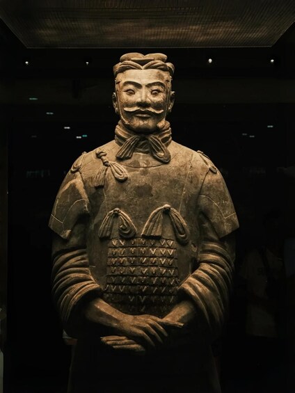 A terracotta statue with a detailed chest plate, standing in a dimly lit room. 4
