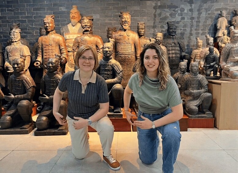 Two people kneeling in front of a collection of bronze statues. 2