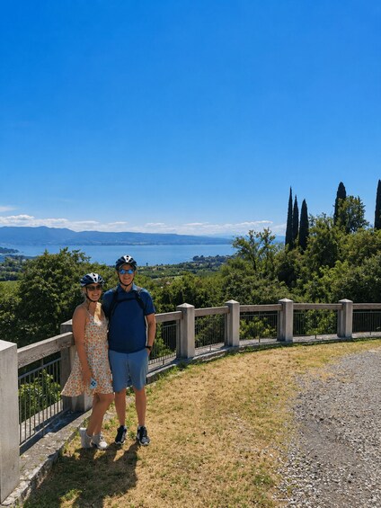 A couple standing on a grassy overlook with a view of a lake and distant mountains. 5