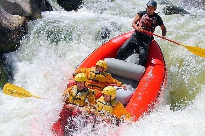 A group of people in a red raft navigating a river with white water rapids. 1