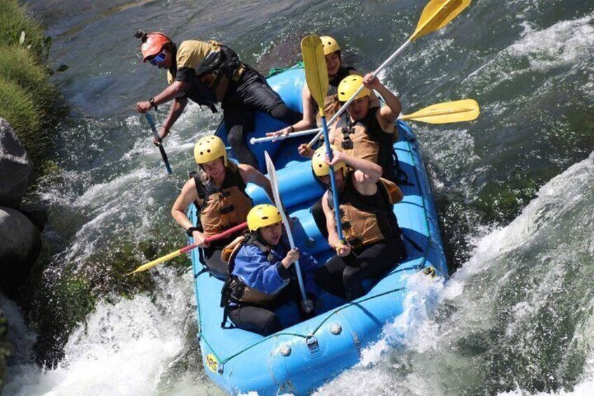 A group of people in a blue raft navigating a river with rapids. 2