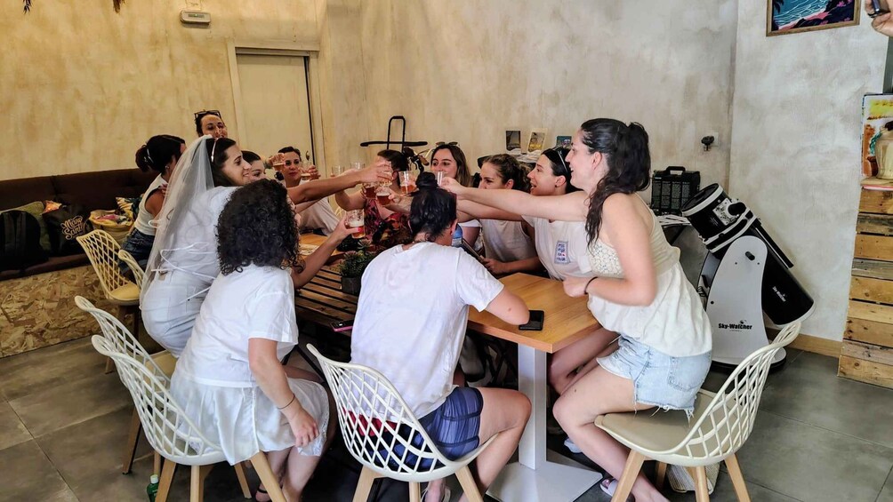 A group of people toasting around a wooden table in a room with a door and a wall-mounted device. 3