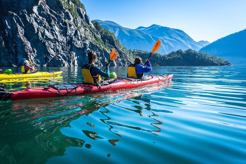 Three kayakers in a red kayak on calm water with mountains in the background. 1