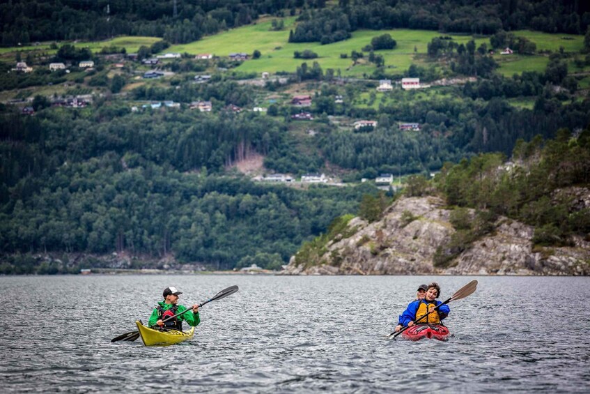 Two kayakers on a calm lake with a backdrop of a hilly landscape and scattered houses. 2