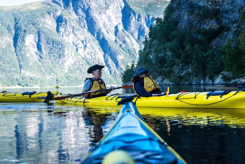 Two people kayaking on a calm river with steep cliffs in the background. 3