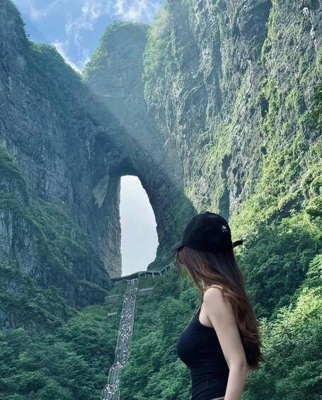 A person standing in front of a natural rock arch formation with a road passing through it. 1