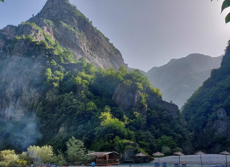 A mountainous landscape with lush greenery, a wooden structure, and a pebble beach. 3