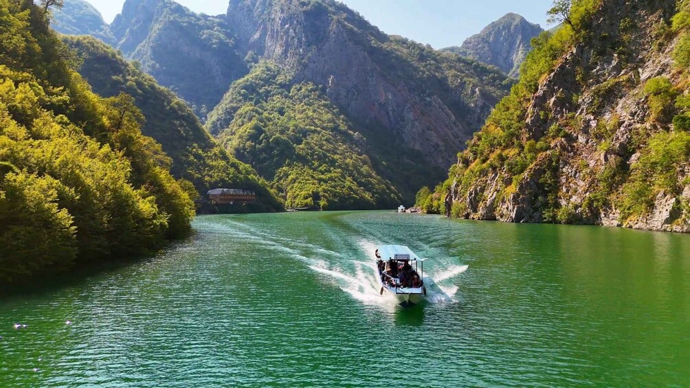 A boat speeding through a green river surrounded by forested mountains. 1