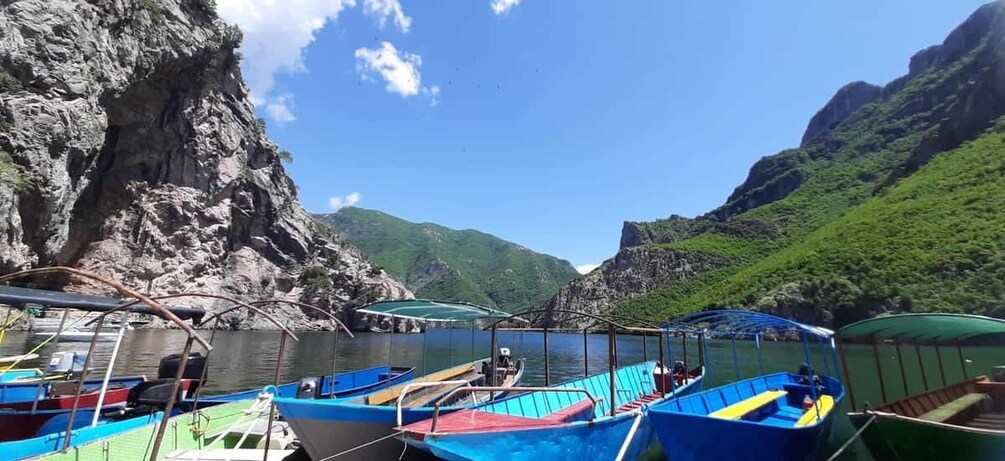 A harbor with boats docked, a rocky cliff, and lush green hills in the background. 2