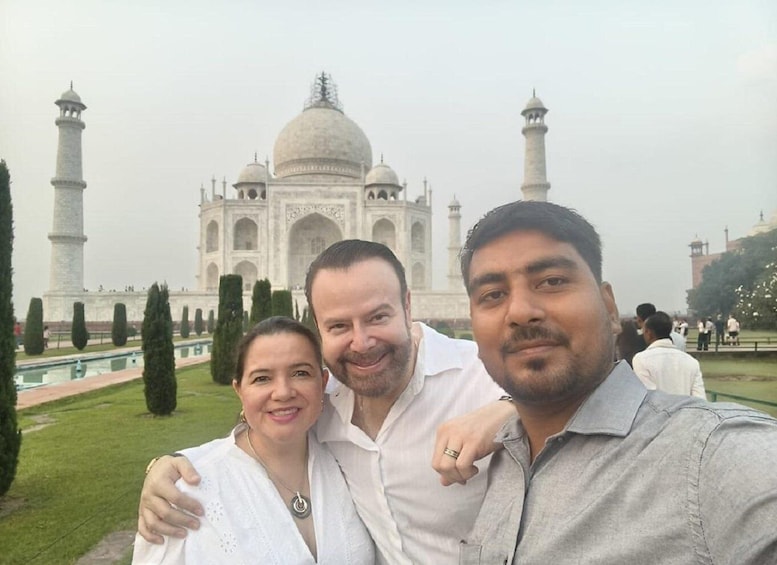 Three people posing in front of the Taj Mahal with its domes and minarets visible. 2