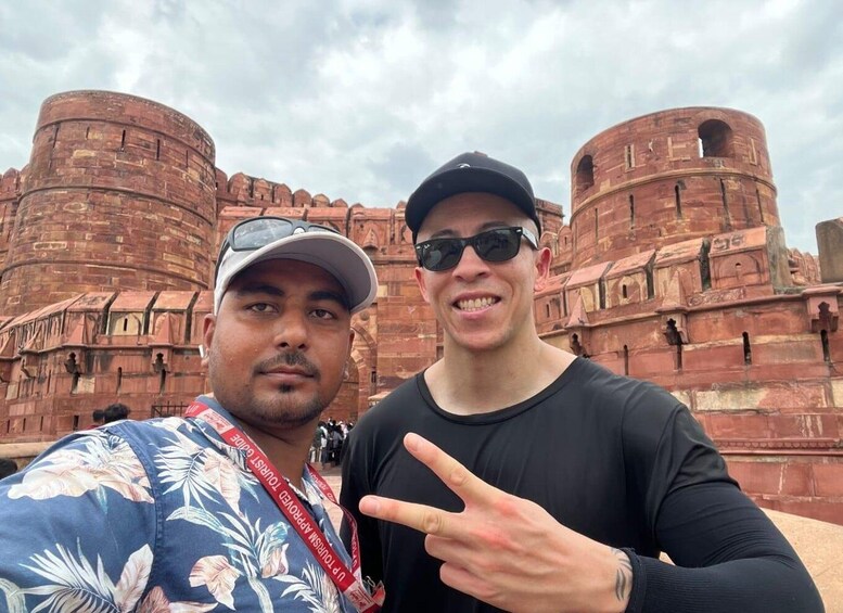 Two people in front of a large, historic red brick building with multiple towers. 5