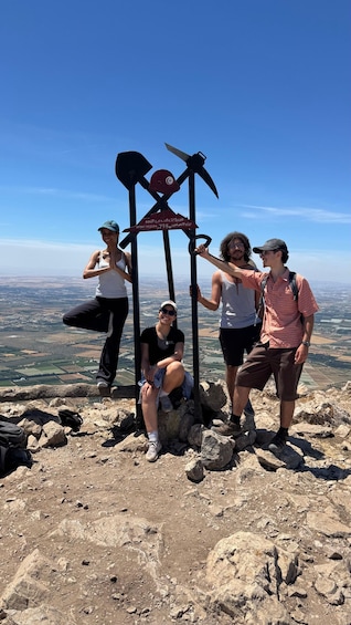 Four people standing on a rocky mountain peak with a metal structure in the center, overlooking a vast landscape. 1