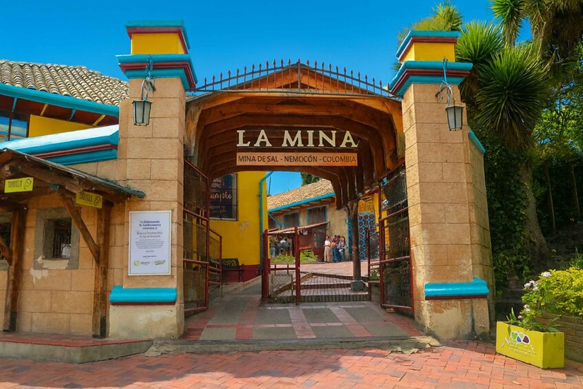 A wooden archway with 'LA MINA' written on it, leading to a building with a tiled roof. 3