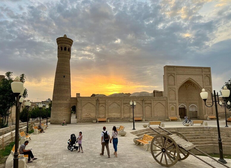 A historic building with a tall minaret and a large courtyard with benches and a wooden cart. 2