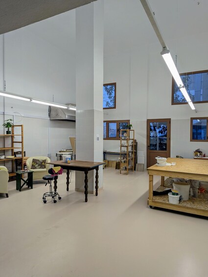 A spacious room with high ceilings, a wooden table, a desk, and shelves with various items. 3