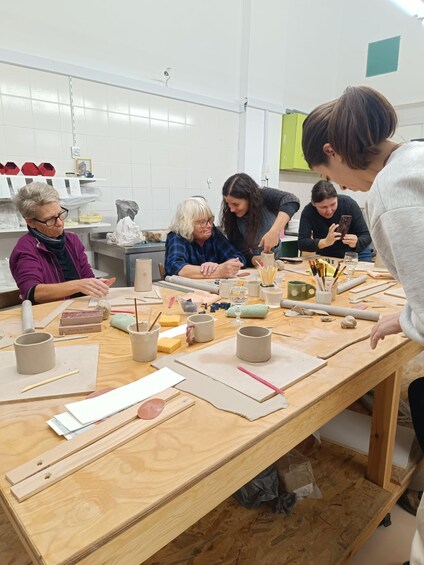 A group of people engaged in pottery making, with various tools, clay, and pottery items on a wooden table. 2