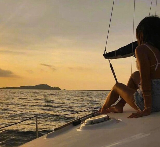 A person sitting on a boat's deck during sunset, with calm waters and distant land visible. 2