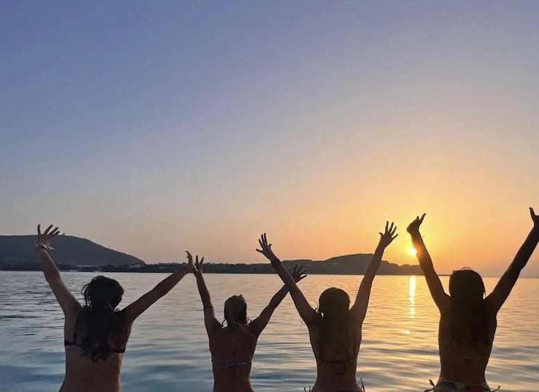 Four people with arms raised, silhouetted against a sunset over water. 1