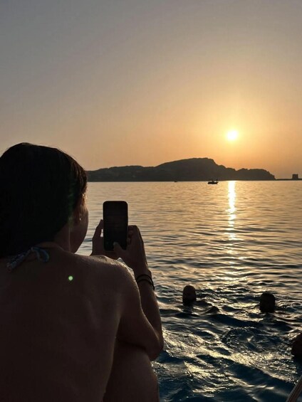 A person taking a photo of a sunset over water with boats. 3