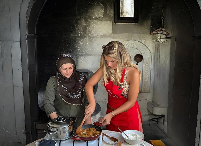 Two people cooking in a rustic kitchen with stone walls and a wooden table. 1