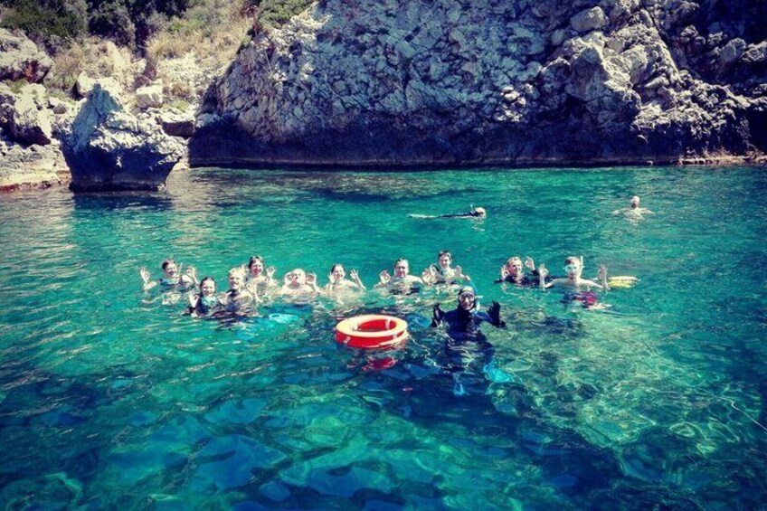 A group of people swimming in clear blue water with a rocky coastline in the background. 4