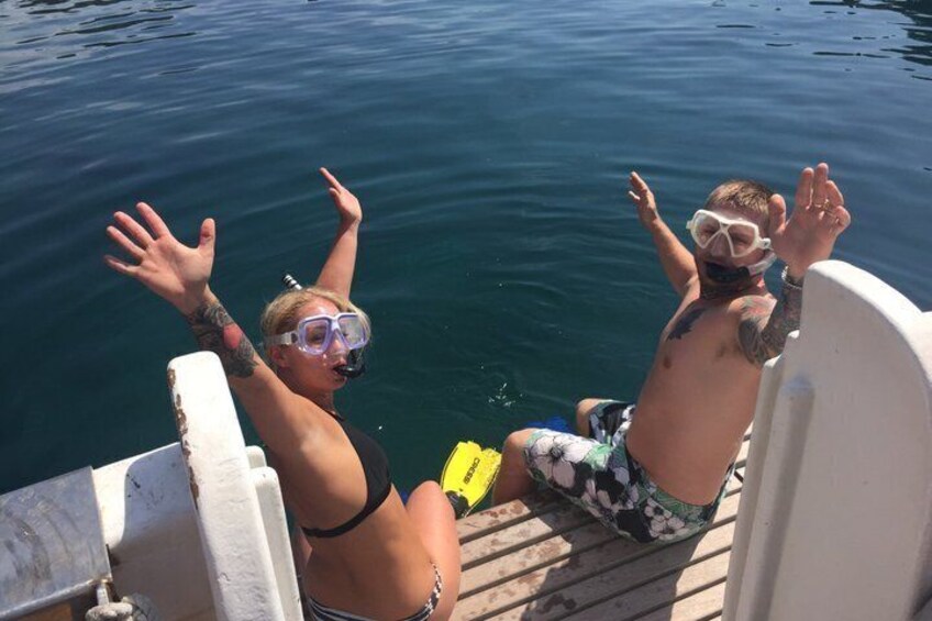 Two people on a boat, one wearing a snorkel mask and the other in swim trunks, with water behind them. 2