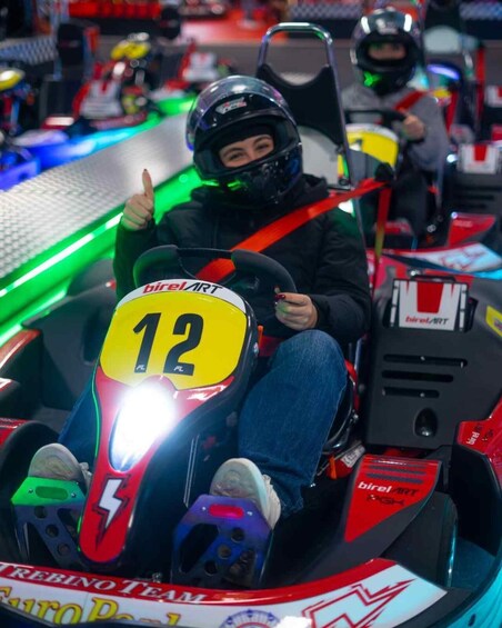A go-kart with the number 12, a driver wearing a helmet, and a track with green and red lighting. 5