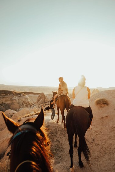 Two people riding horses in a desert landscape with rocky terrain and sparse vegetation. 5