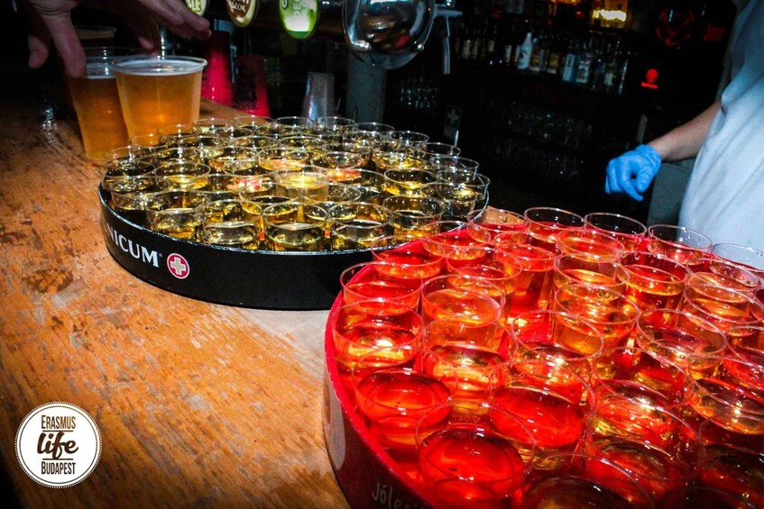 A bar with shot glasses filled with amber liquid, a beer tap, and a person wearing a blue glove. 2