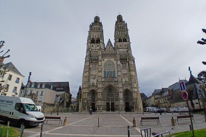 A Gothic cathedral with two towers, a paved square, and parked cars. 1
