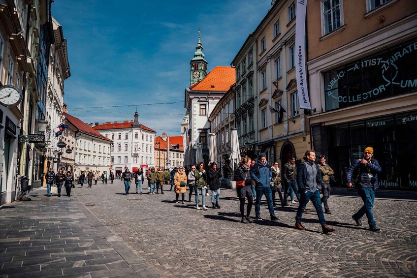 A cobblestone street lined with historic buildings, a prominent church tower, and a public artist store. 1